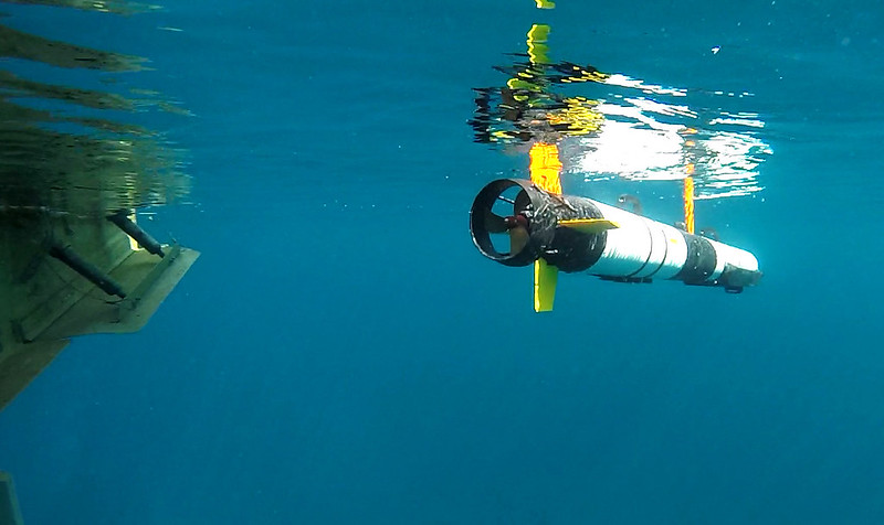 Underwater autonomous vehicle waits for instructions next to the hull of a boat under the lake's surface